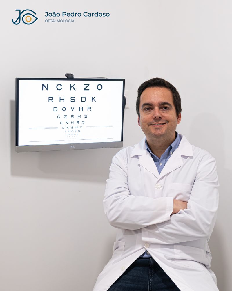 O Dr. João Pedro Cardoso no consultório, junto a uma tabela optométrica